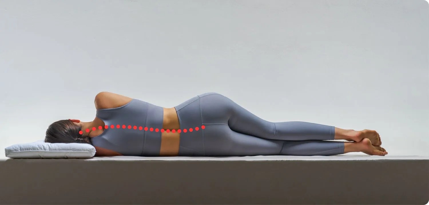 A person lying on their side on a firm mattress, a dotted red line marking the axis of the body at the shoulder