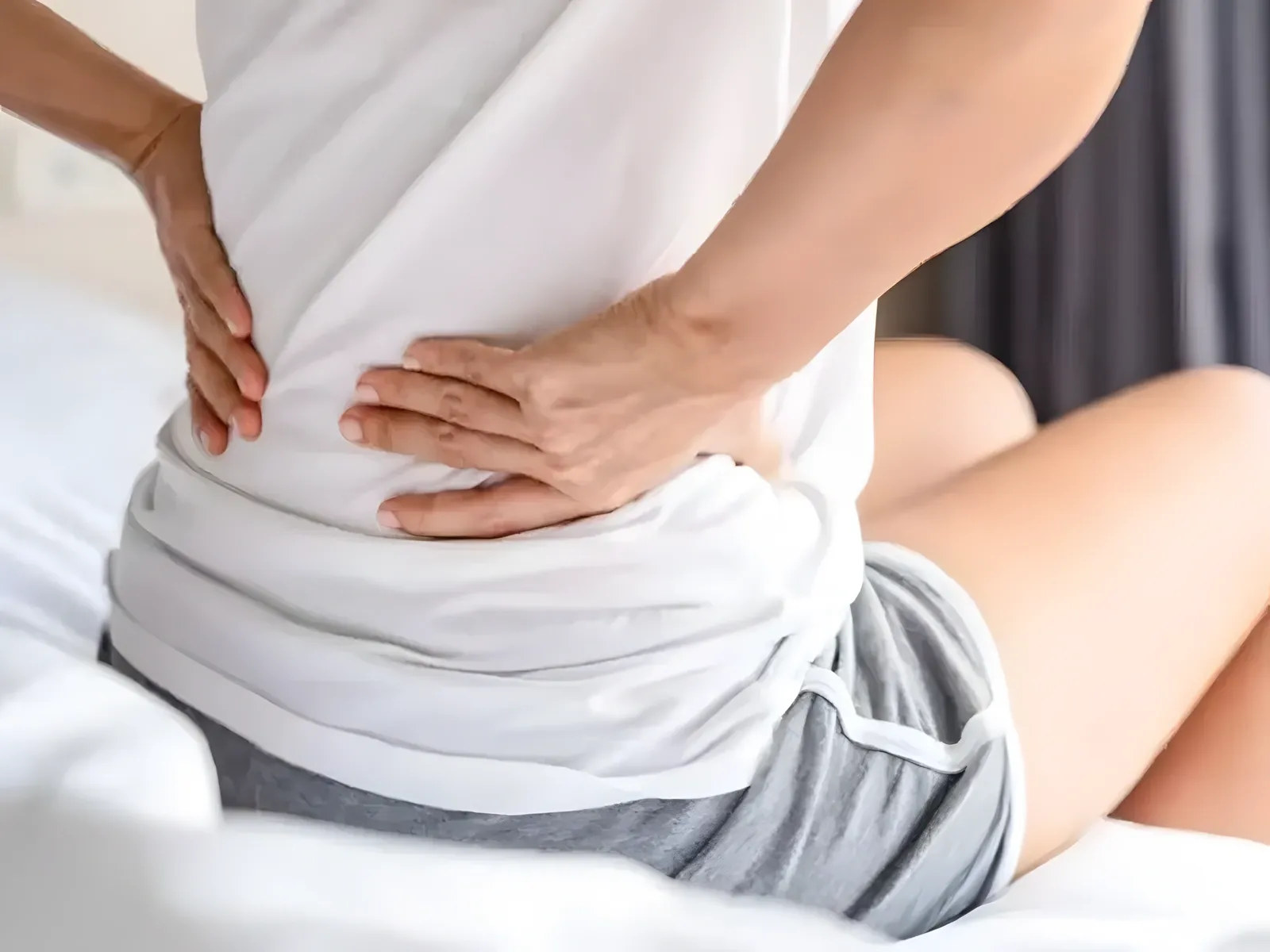 Người phụ nữ ngồi trên giường, hai tay ôm vùng lưng dưới