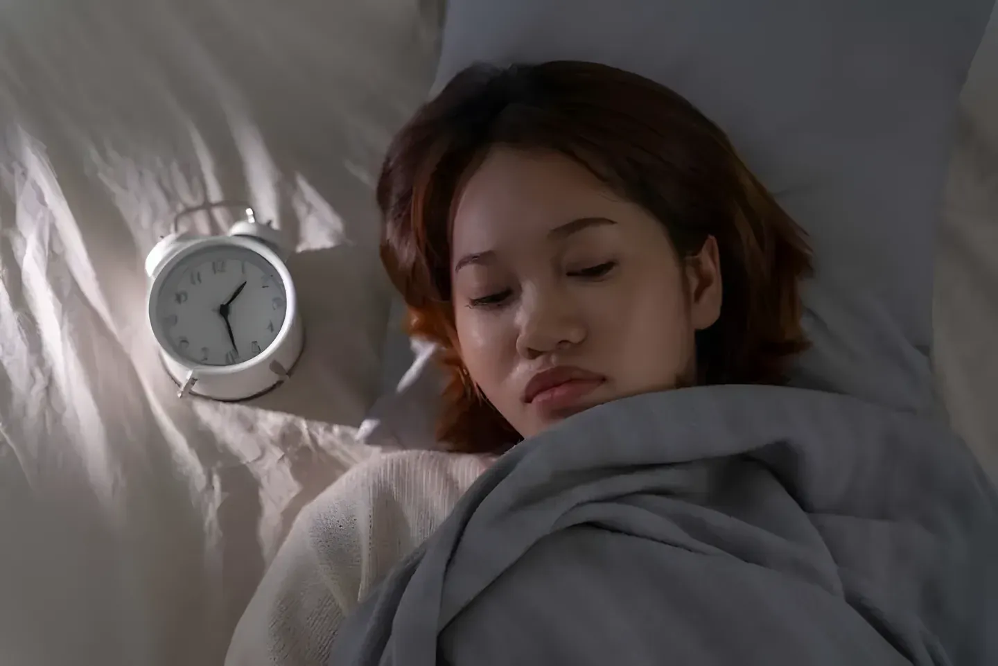 Cô gái nhắm mắt ngủ cạnh chiếc đồng hồ báo thức trong phòng tối