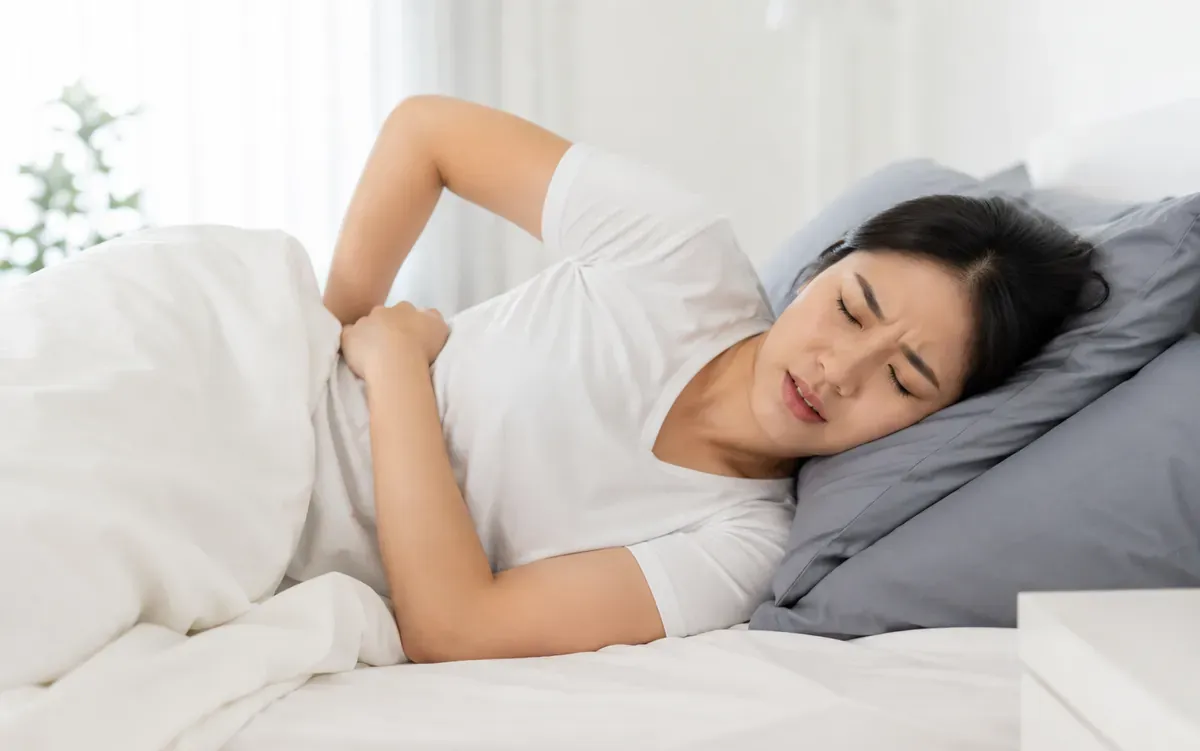 Người phụ nữ nằm nghiêng ôm lưng vì đau mỏi trên giường