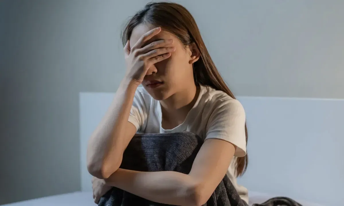 Cô gái ngồi trên giường, ôm đầu mệt mỏi sau đêm mơ nhiều