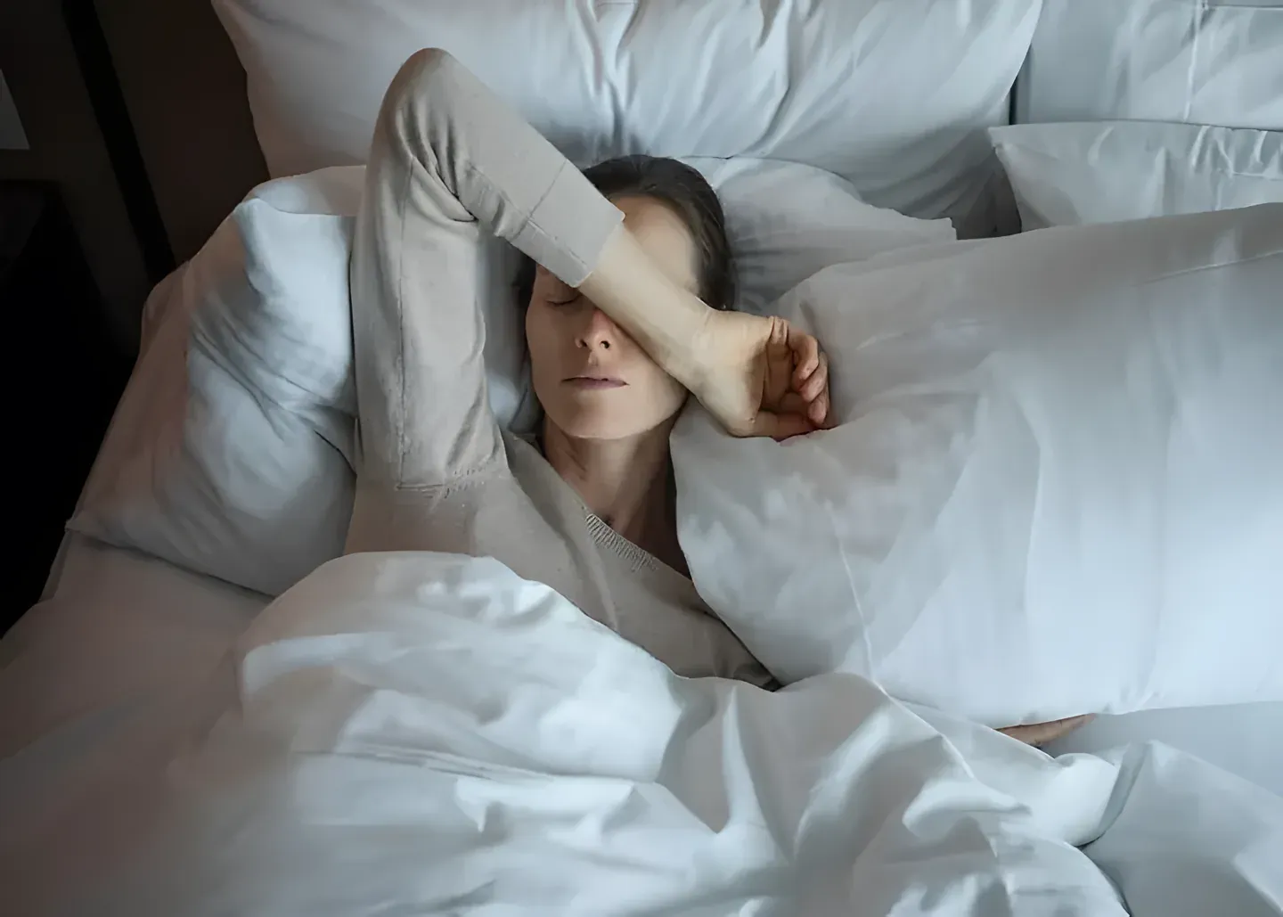 Người phụ nữ nằm trên giường, lấy tay che mắt vì mệt mỏi sau đêm ngủ chập chờn